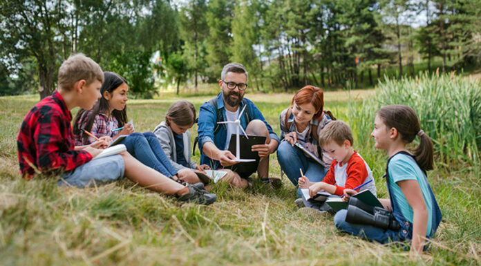 Group of school children with teacher and windmill model on field trip in nature.